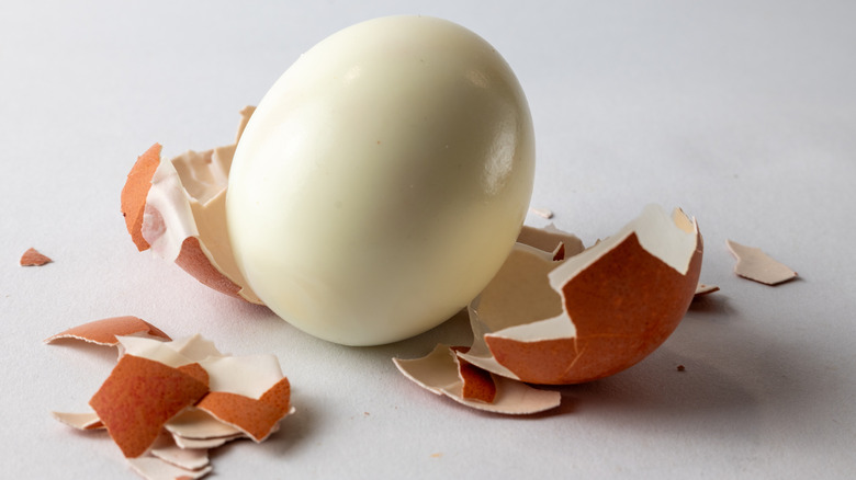 A hard-boiled egg peeled, the brown shell sitting to the side, peeled in large pieces.