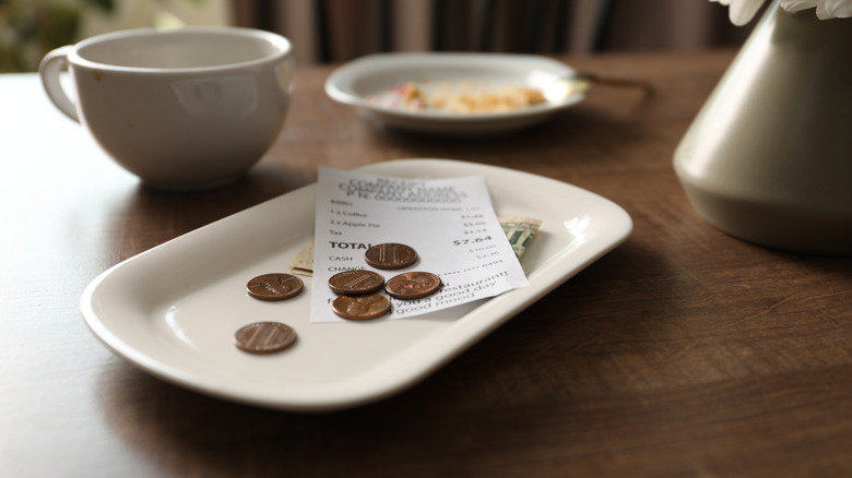 A check sits on a table at a restaurant, with bills underneath and pennies on top.