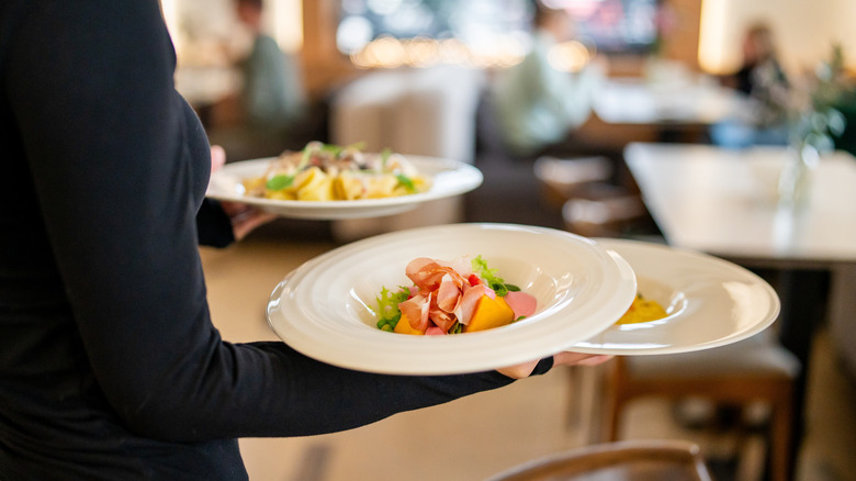 Server inside restaurant carrying several plates of food.