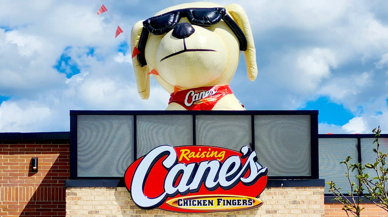 Raising Cane's sign in front of restaurant with inflatable dog in sunglasses