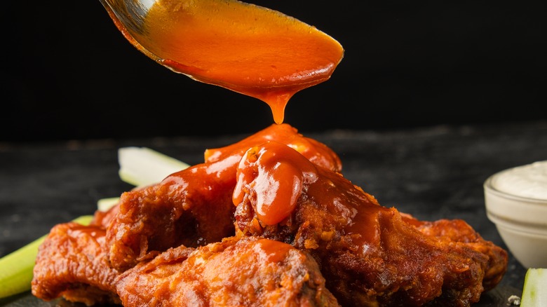 hot sauce being spooned onto chicken wings
