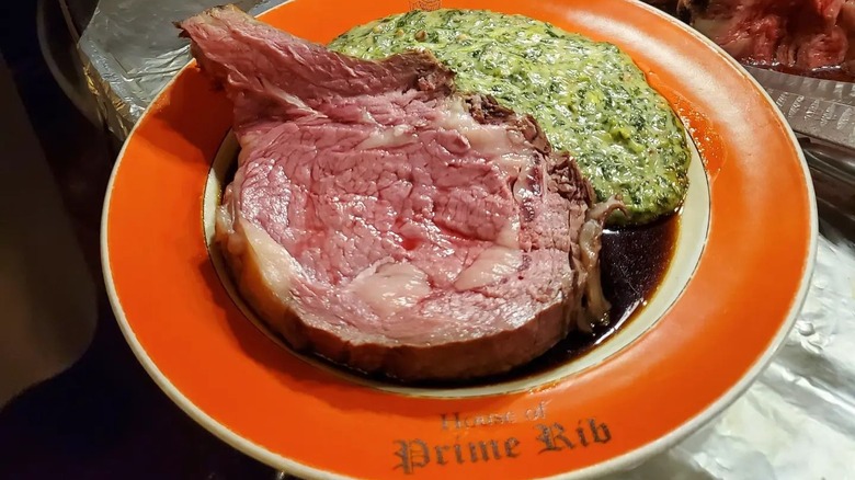 A thick slice of prime rib with creamed spinach on the side on a House of Prime Rib plate.