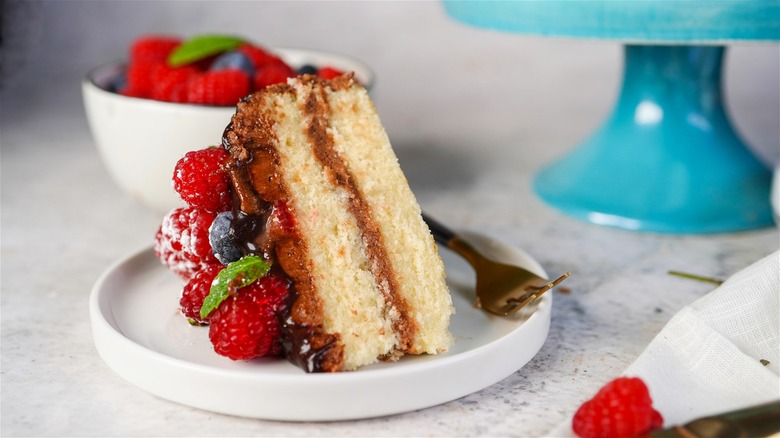 A slice of homemade vanilla sponge cake with chocolate buttercream frosting topped with fresh berries