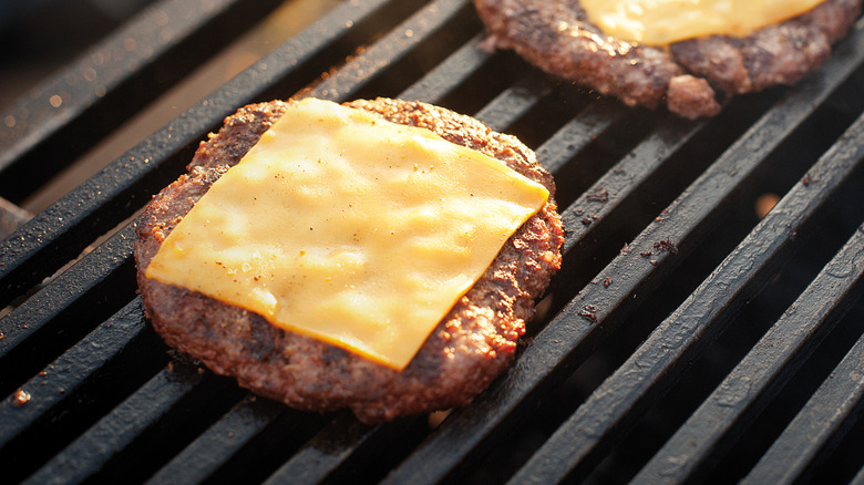 Beef patties with melted cheese on a grill.
