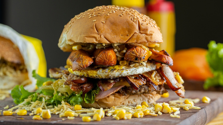 A Brazilian X-tudo burger surrounded by corn kernels.