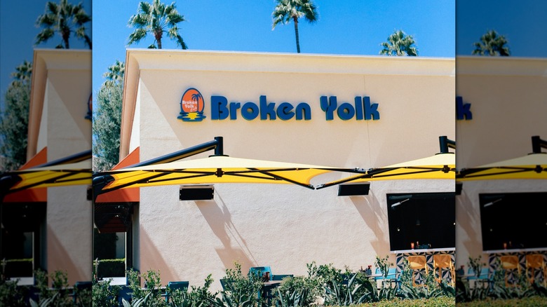 Exterior entrance of Broken Yolk cafe restaurant with big yellow umbrellas over outdoor tables