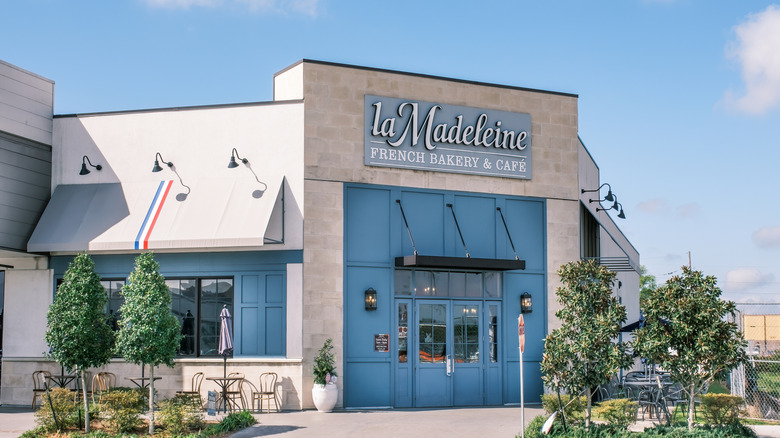 exterior entrance of la madeleine bakery restaurant with landscaping and outdoor patio tables