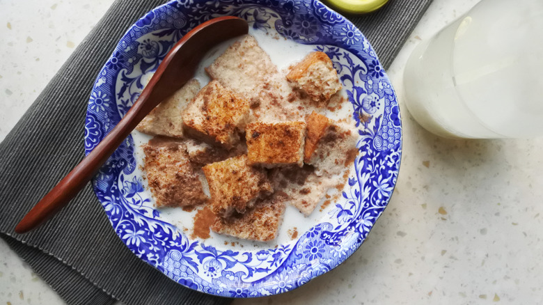 Blue bowl of milk toast with glass of milk and a spoon
