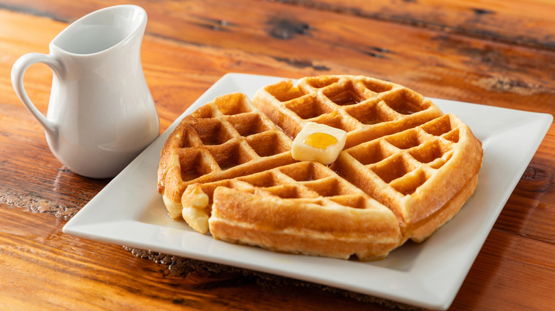 A plate of butter-topped waffle wedges with a jug of syrup
