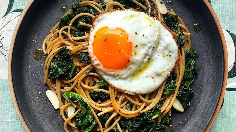 plate of spaghetti with kale and a sunny side up egg