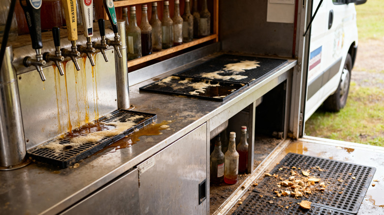 A beer tap area in a mobile unit shows overflowing drip trays and an unsanitary counter space.