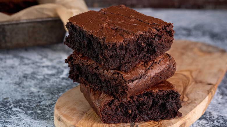 3 brownies stacked upon each other on top of a wooden plate and a blue marble counter