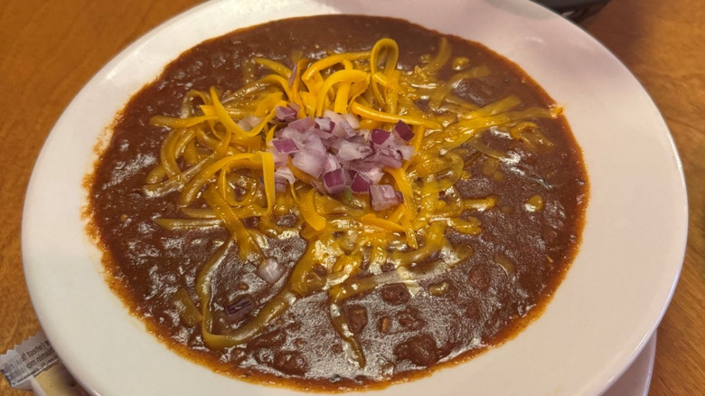 Texas Roadhouse chili with beans, cheese, and onions on wooden table