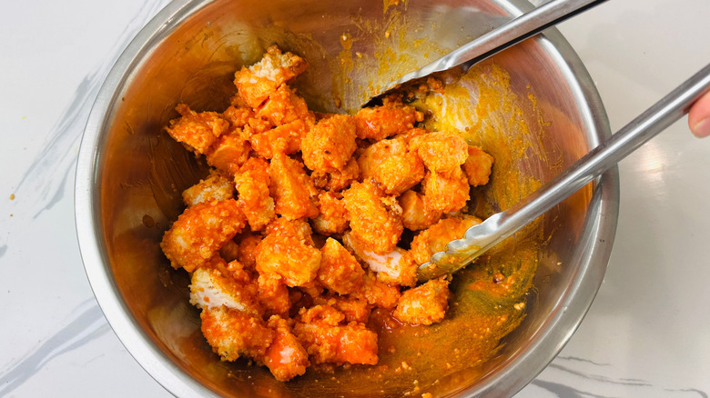 Tongs tossing Buffalo chicken in bowl