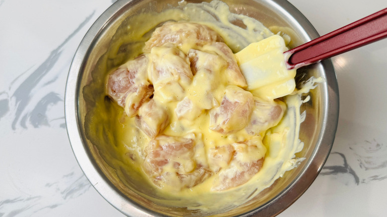 Raw chicken cubes coated in egg mixture in bowl