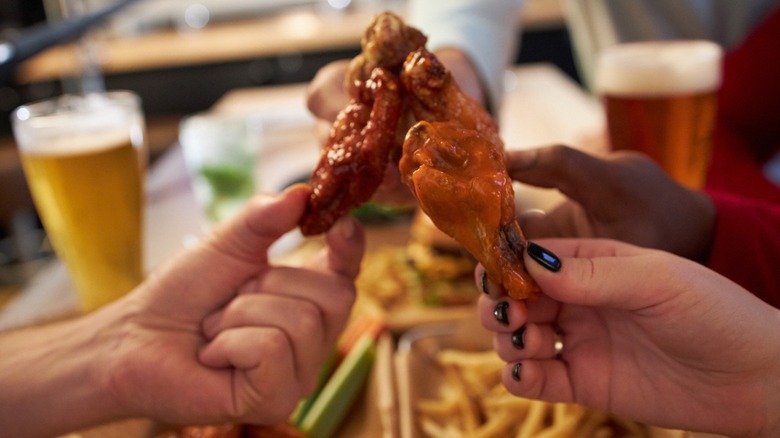People holding wings from Buffalo Wild Wings over french fries.