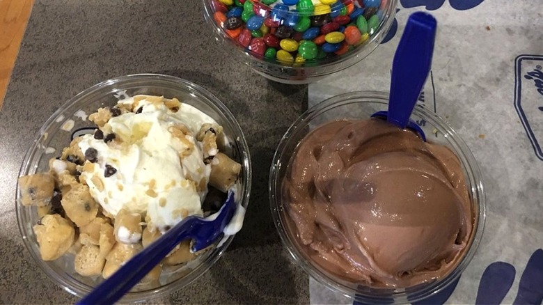 Two frozen custard desserts, one with mix-ins and one chocolate, with one in background with candies.