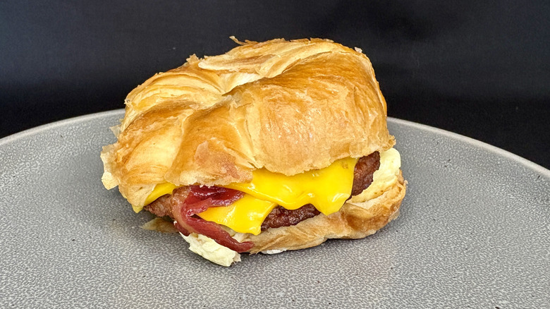 Bacon, sausage, egg, and cheese croissant sandwich on gray plate