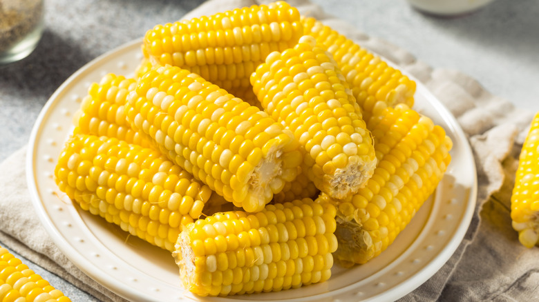 Boiled corn on the cob stacked on white plate.