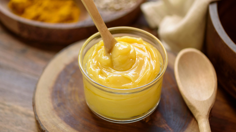 A glass jar of ghee butter on a wooden tray with wooden spoon