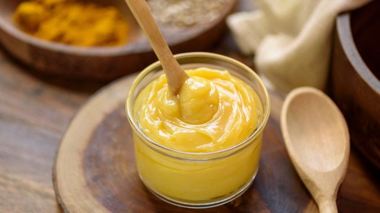 A glass jar of ghee butter on a wooden tray with wooden spoon