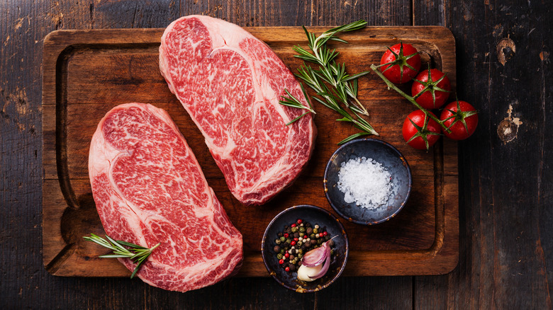Two well-marbled steaks on cutting board with seasonings