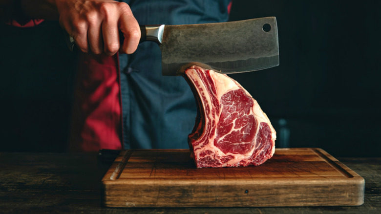 Butcher carving a well-marbled prime rib steak on wood cutting board