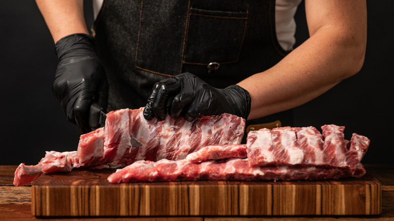 Butcher preparing deep red colored pork ribs on a wooden cutting board