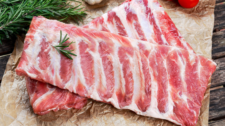 Pork ribs with even fat marbling on a sheet of butcher paper surrounded by herbs