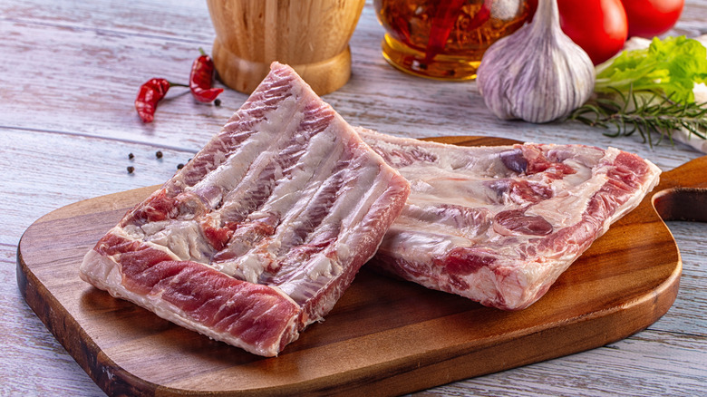 Raw pork ribs on a wooden cutting board with vegetables in the background