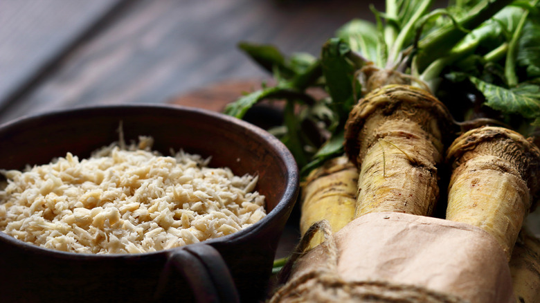 Grated horseradish in a bowl next to whole horseradish