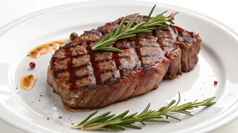 Grilled ribeye with sprigs of rosemary on white plate