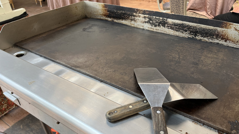 An empty flat top grill with two spatulas
