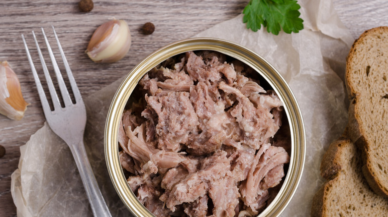 Opened can of chicken with fork, bread, and garlic cloves