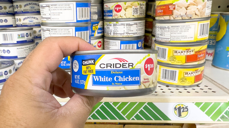 A hand holding up a can of chicken at a grocery store