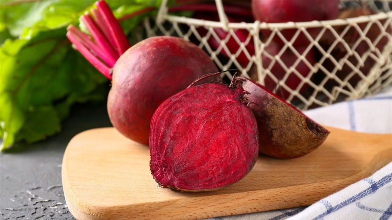 A sliced raw beet on a wooden board, with beet greens in the background.