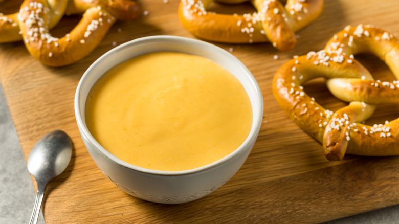 White bowl of yellow beer cheese dip with soft pretzels on wooden cutting board.