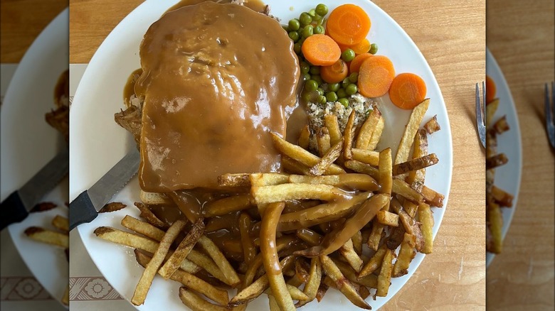 Hot hamburg sandwich plated with fries, peas, and carrots.