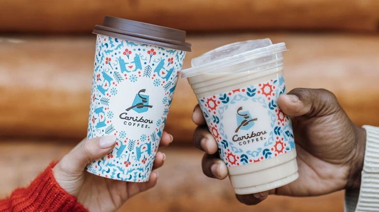 two people holding hot and cold Caribou Coffee holiday beverages