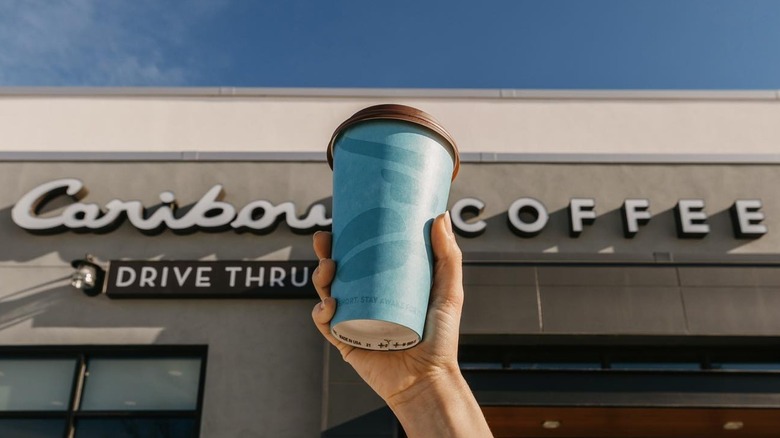 Hand holding a coffee against a Caribou Coffee sign