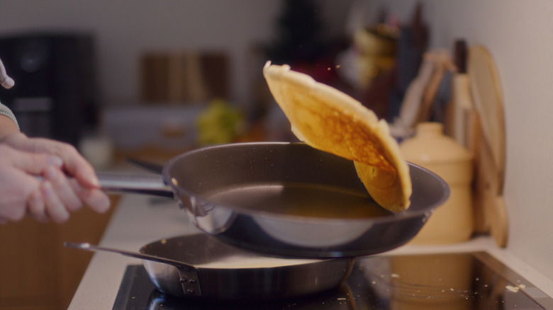 hands holding a handle of a nonstick pan, tossing a pancake