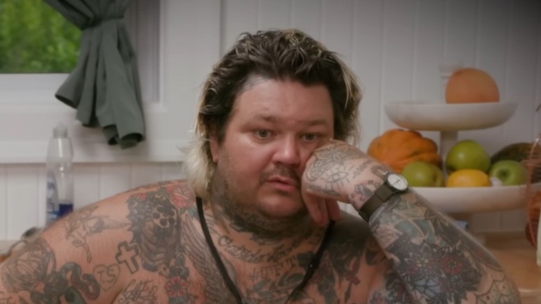 Matty Matheson sits glumly in a kitchen, shirtless while resting his left cheek on his left knuckles, a large bowl of soup before him