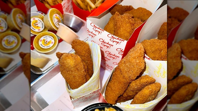 Several orders of chicken tenders in to-go containers with assorted sauces and side dishes, including fries and mac and cheese