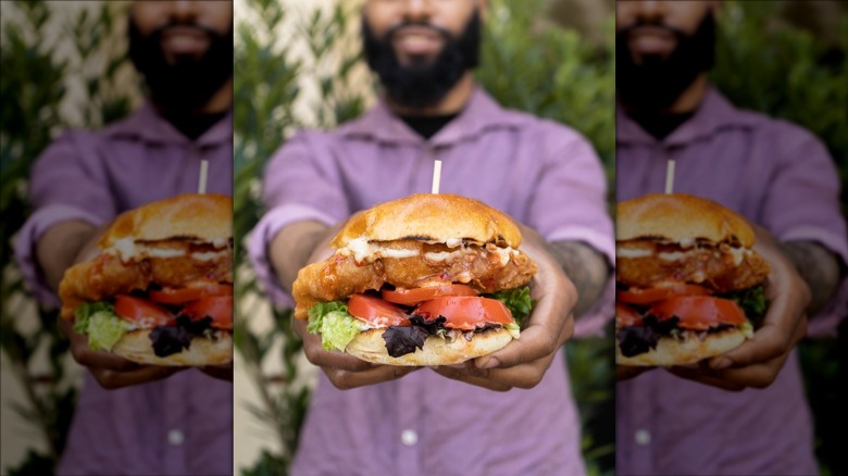 Man in purple shirt holding out a fish sandwich