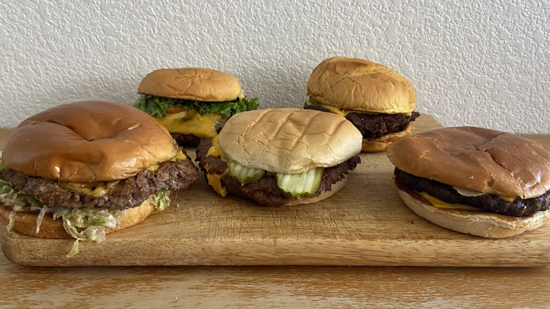 Assorted fast food smash burgers on wooden cutting board.