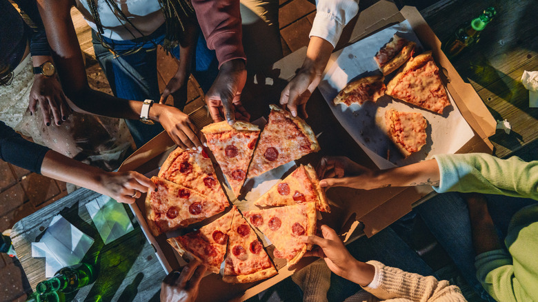 Group of friends pulling slices of pizza from box