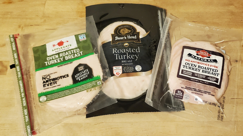 three expensive brands of deli turkey in packaging on wooden surface, including Boar's Head, Applegate, and Dietz and Watson