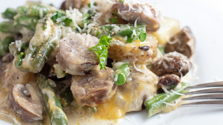 Close up of a plate of cheesy bratwurst casserole and the prongs of a metal fork