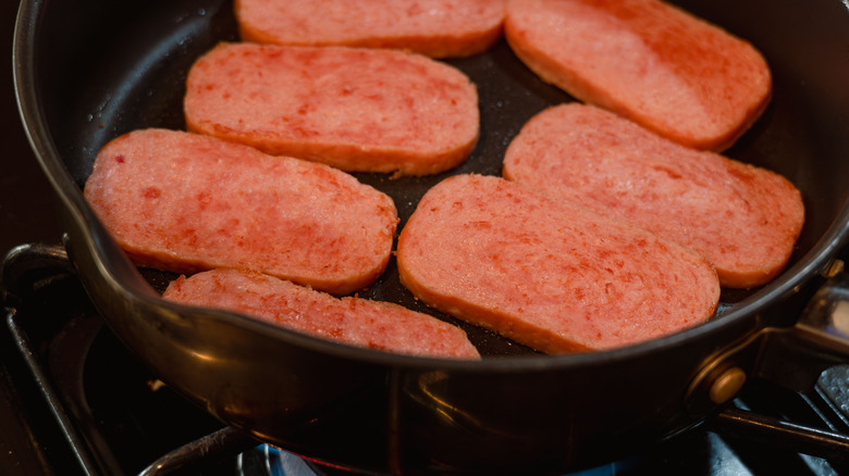 Slices of Spam frying cast-iron pan
