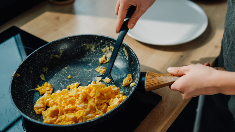 Closeup of hands cooking scrambled eggs on stove top